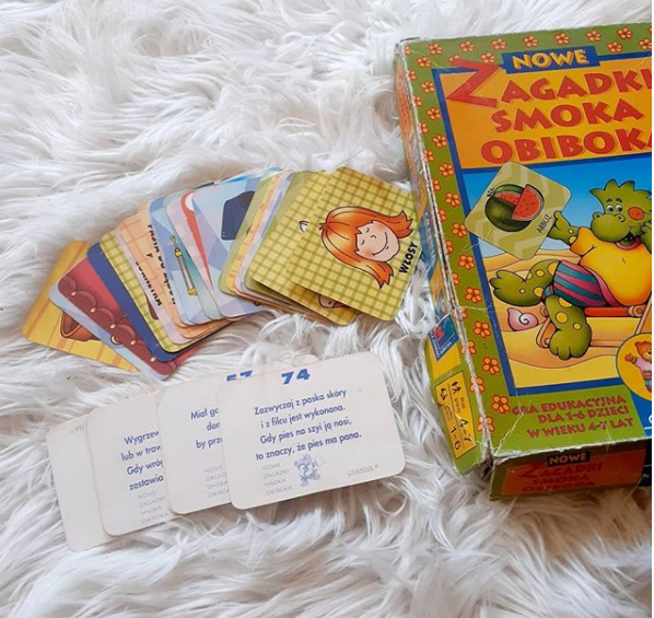 Pudełko "Zagadki Smoka Obiboka" obok kilka kart z obrazkami i kilka odwróconych kart z zapisanymi zagadkami.